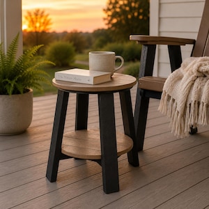May include: A round side table with a tan top and shelf supported by four black legs. A beige ceramic mug and a book titled The Nature Home rest on the surface. The table is constructed with a two-tone design featuring a circular top and base.