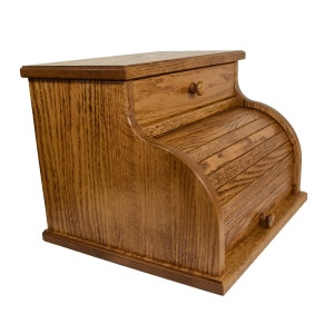 May include: A wooden bread box with a roll-top door and a drawer. The bread box is made of oak and has a natural finish. The roll-top door slides up and down, and the drawer has a small wooden knob. The bread box is a classic kitchen storage item.
