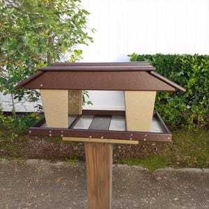 May include: A brown and beige bird feeder with a roof and two feeding stations. The feeder is mounted on a wooden post.