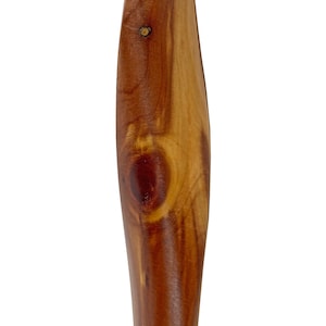 May include: Close-up of a wooden object with a smooth, curved design. The wood grain is visible, showcasing a mix of light and dark brown tones. A small knot and a pin are present, adding texture to the surface.