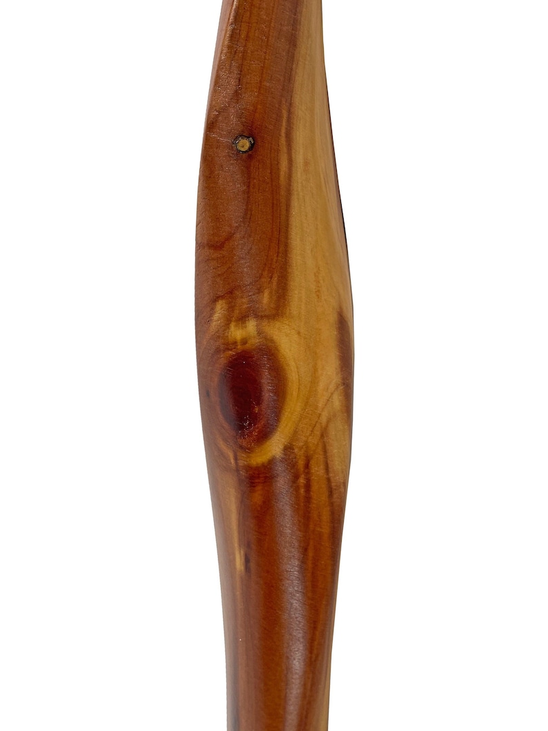 May include: Close-up of a wooden object with a smooth, curved design. The wood grain is visible, showcasing a mix of light and dark brown tones. A small knot and a pin are present, adding texture to the surface.
