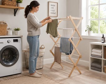 May include: A light-colored wooden accordion-style laundry drying rack with multiple horizontal rungs. The rack is freestanding and features an expandable scissor-like frame design, currently holding several pieces of clothing including a green shirt.