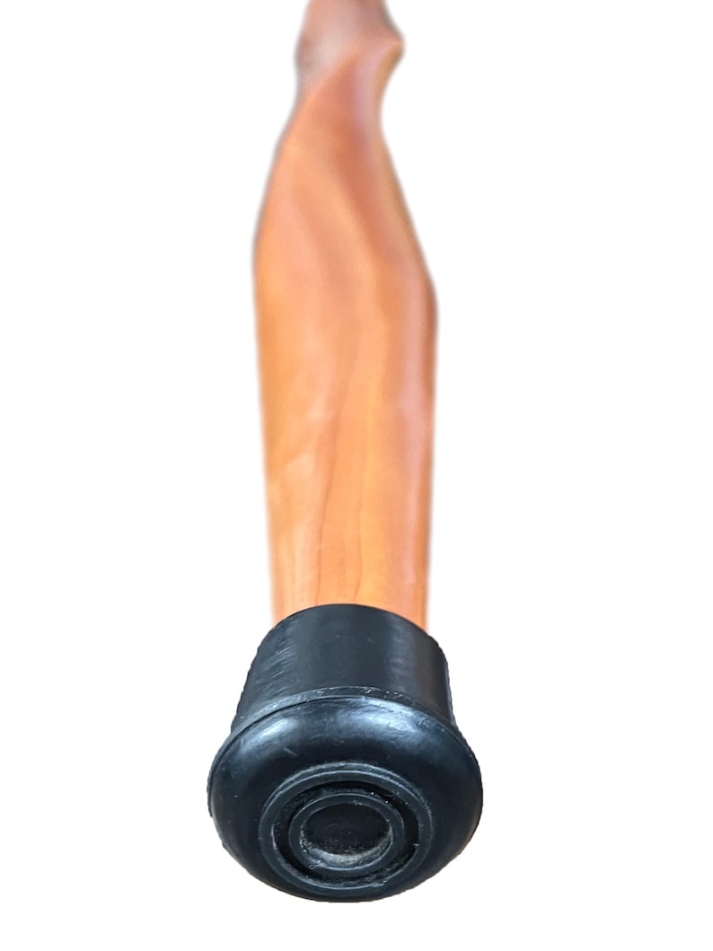 May include: A wooden walking cane with a light brown finish. The cane has a curved handle and a black rubber tip for stability. The cane is designed for support and mobility.