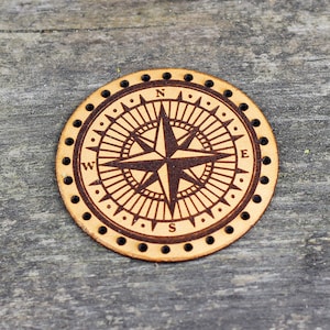 May include: A round, leather compass with a brown background and a black compass rose. The compass is engraved with the letters N, S, E, and W.