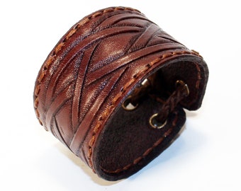 May include: A brown leather cuff bracelet with a woven design and stitching. The cuff has a buckle closure.