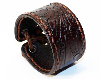 May include: A brown leather bracelet with a decorative stitched pattern. The bracelet has a buckle closure and is made of a thick, durable leather.
