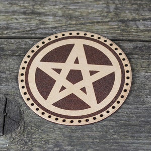 May include: A brown leather coaster with a white pentagram design. The coaster has a decorative border of small black dots.