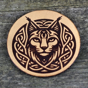 May include: A round leather patch with a brown background and a black and white design of a lynx head inside a Celtic knot pattern.