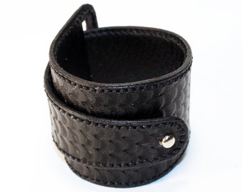 May include: A black leather cuff bracelet with a textured pattern and a silver snap closure.