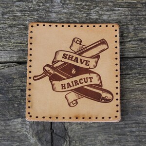 May include: A brown leather patch with a vintage-style illustration of a straight razor and a ribbon that reads "SHAVE & HAIRCUT".