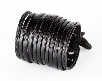 May include: Black leather bracelet with multiple layers of leather woven together. The bracelet has a tie closure.
