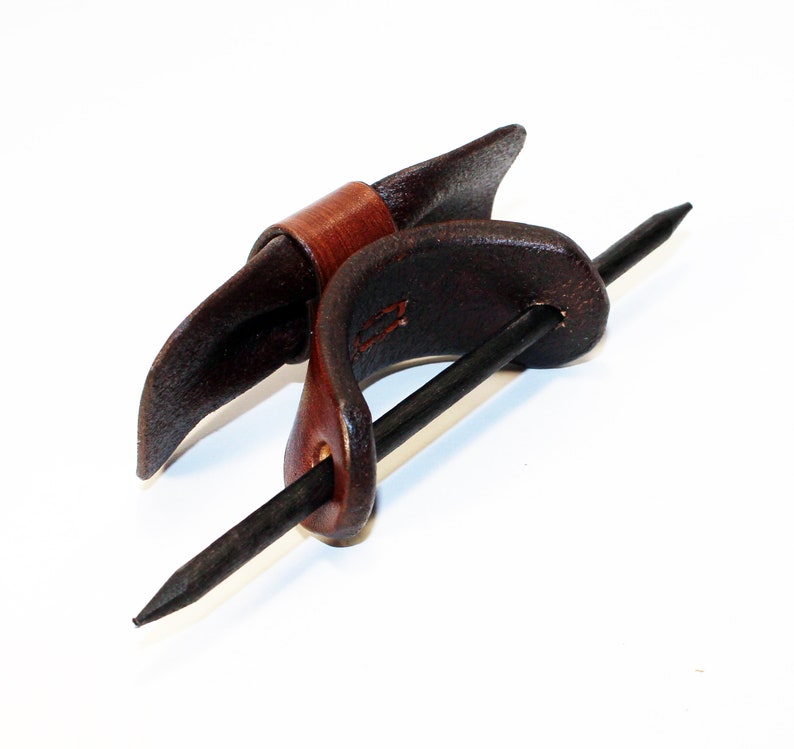 May include: A brown leather hair stick with a dark brown leather wrap. The stick is made of metal and has a pointed end.