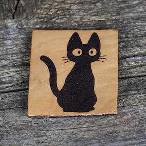 Puede incluir: Un posavasos de cuero marrón claro con la silueta de un gato negro grabada con láser.