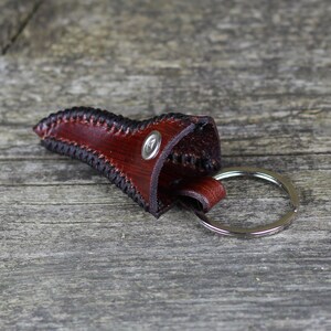 May include: A brown leather key chain with a stitched edge and a silver ring. The leather is folded over to create a small pouch.