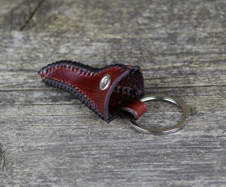 May include: A brown leather key chain with a stitched edge and a silver ring. The leather is folded over to create a small pouch.