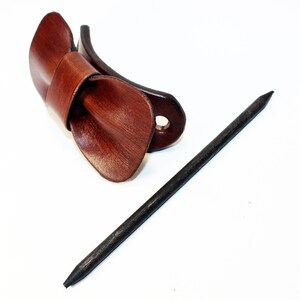 May include: A brown leather hair clip with a bow shape and a black wooden hair stick.