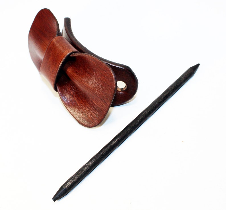 May include: A brown leather hair clip with a bow shape and a black wooden hair stick.
