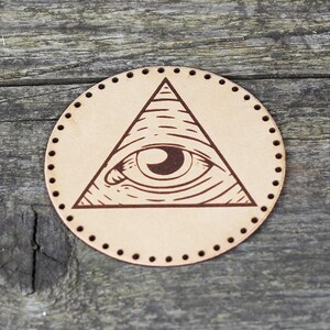 May include: A brown leather patch with a stitched edge, featuring a brown all-seeing eye inside a triangle.