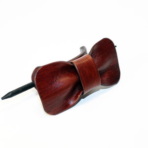 May include: A brown leather hair stick with a bow shape. The stick is made of metal and is black.