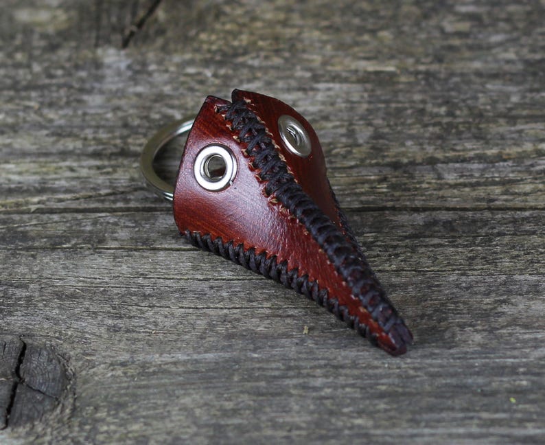 May include: A brown leather plague doctor mask keychain with black stitching and a silver metal ring.