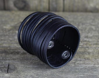 May include: A black leather cuff bracelet with multiple layers and two silver snap closures.