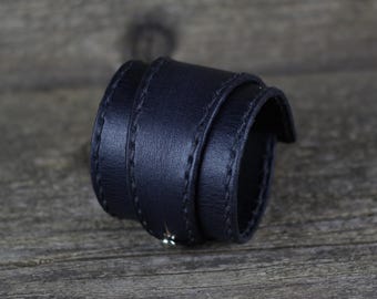 May include: A black leather cuff bracelet with a stitched design.
