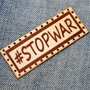 May include: A brown leather patch with a white background and the text "#STOPWAR" in brown lettering.
