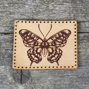May include: A brown leather patch with a detailed butterfly design. The butterfly is brown and black with intricate markings. The patch has a stitched border.