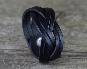 May include: A black leather bracelet with a braided design. The bracelet is made of multiple strands of leather that are woven together.