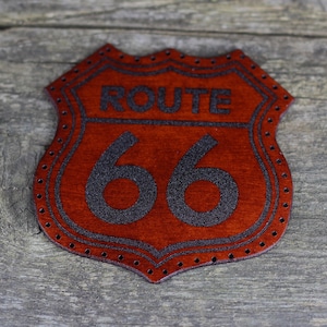 Puede incluir: Un parche de cuero marrón con un contorno negro y el texto "ROUTE 66" en negro.
