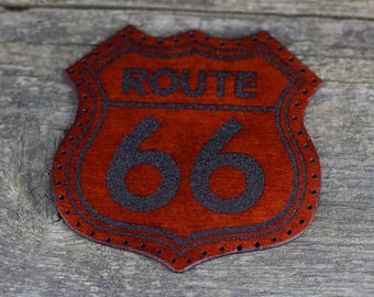 Pode incluir: Um remendo de couro marrom com contorno preto e o texto "ROUTE 66" em preto.