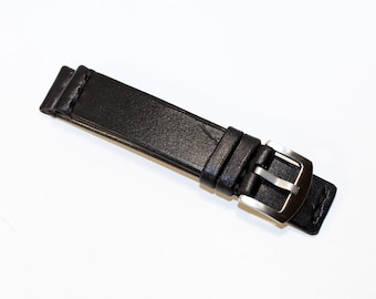 May include: A black leather watch strap with a silver-colored buckle. The strap is made of textured leather and has a classic design. The buckle is rectangular and has a brushed metal finish.