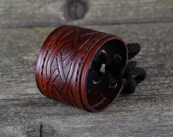 May include: A brown leather bracelet with a Celtic knot design and a black cord closure.