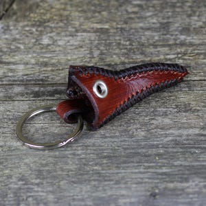 May include: A brown leather key chain with a stitched black border and a metal ring. The leather is shaped like a pointed tip.