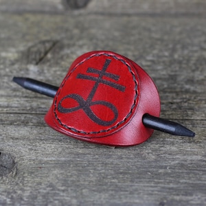 May include: A red leather hair stick with a black infinity symbol and cross design.