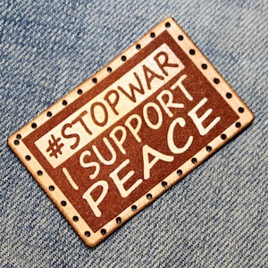 May include: A brown leather patch with white stitching and the text "#STOPWAR I SUPPORT PEACE" in white lettering.