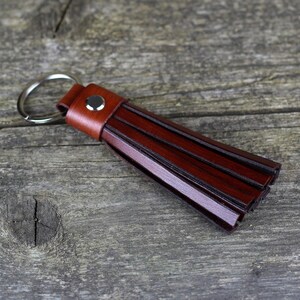 Peut inclure: Un porte-clés en cuir marron avec un anneau argenté. Le pompon est composé de plusieurs lanières de cuir.