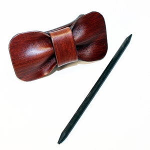 May include: A brown leather bow tie hair clip with a black wooden stick.