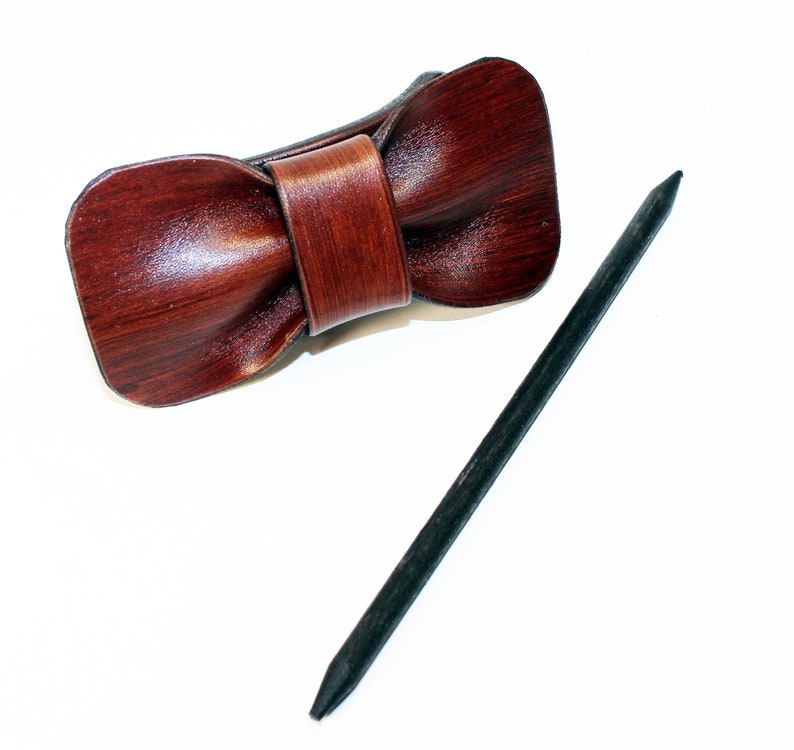 May include: A brown leather bow tie hair clip with a black wooden stick.