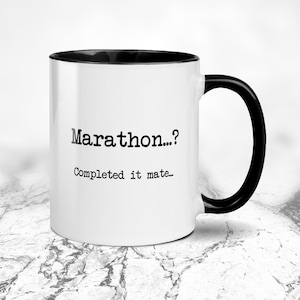 K&ouml;nnte beinhalten: Wei&szlig;er Keramikbecher mit schwarzem Innenraum und Henkel. Der Becher tr&auml;gt den Text "Marathon...?" &uuml;ber "Completed it mate..." in schwarzer Schrift. Auf einer marmor&auml;hnlichen Oberfl&auml;che.