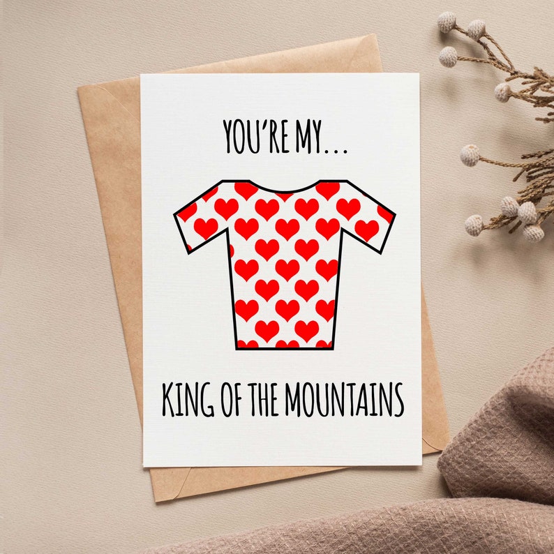 May include: Greeting card with a white background and a brown envelope. The card features a red heart-patterned jersey graphic and the text "YOU'RE MY... KING OF THE MOUNTAINS" in black.