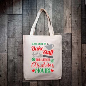 May include: Cream-colored tote bag with the text "I just want to Bake Stuff and watch Christmas Movies" in red and green. The design includes a whisk, mixing bowl, snowflakes, and hearts. The bag has two handles.