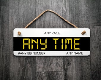 May include: White sign with black background and yellow text that reads "ANY RACE ANY TIME #ANY BIB NUMBER ANY NAME".