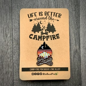 May include: Campfire pin badge with a black and orange enamel design of a campfire with mountains and a crescent moon. The text "Life is better around the campfire" is printed on the brown card backing. The badge is made of zinc alloy.