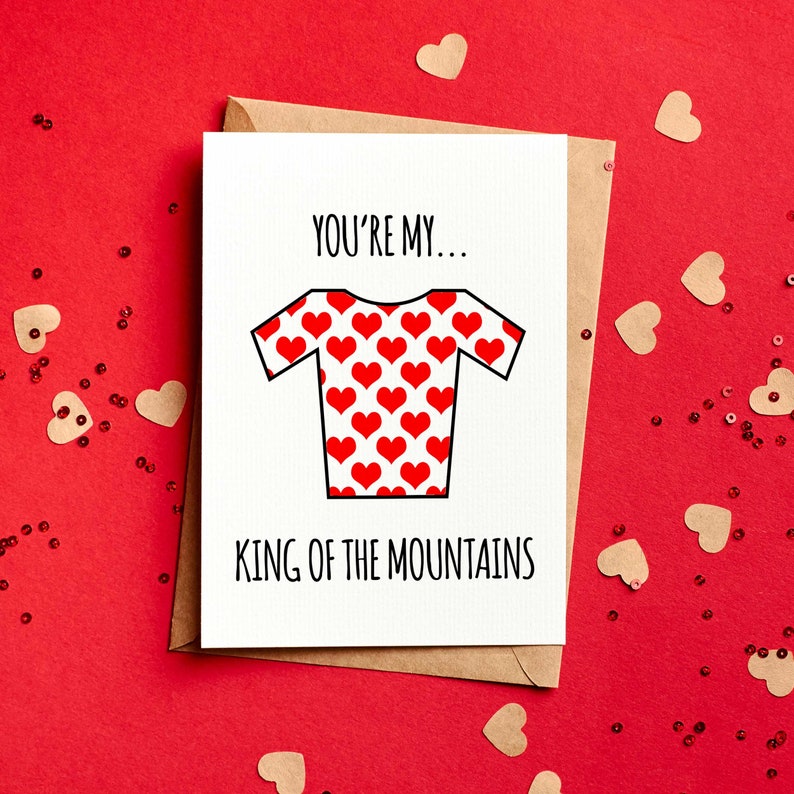 May include: A greeting card with a white background and a brown envelope. The card features a red and white jersey design covered in red hearts. The text reads "YOU'RE MY... KING OF THE MOUNTAINS" in black.