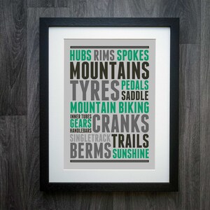 May include: A framed print with a gray background and black text. The text is arranged in a word cloud and includes the words "Hubs, Rims, Spokes, Mountains, Tyres, Pedals, Saddle, Mountain Biking, Inner Tubes, Gears, Cranks, Handlebar, Singletrack, Trails, Berms, Sunshine".