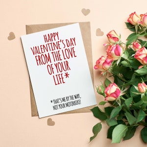 K&ouml;nnte beinhalten: Eine wei&szlig;e Karte mit rotem Text, der "Happy Valentine's Day from the love of your life* *That's me by the way, not your motorbike!" lautet. Die Karte ist von rosa Rosen und braunen Papierherzen umgeben.