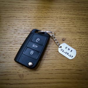 May include: A black car key with a silver keychain attached. The keychain has a silver tag with the text "C & S 02.09.17" engraved on it.