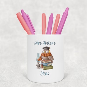 May include: White ceramic pencil holder with an owl wearing a graduation cap and holding a book. The text "Mrs. Foster's Pens" is printed on the holder.