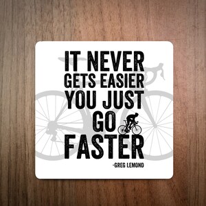 Może przedstawiać: Biały podkładka z czarno-białym obrazkiem kolarza jadącego na rowerze. Tekst brzmi "It never gets easier you just go faster - Greg Lemond".